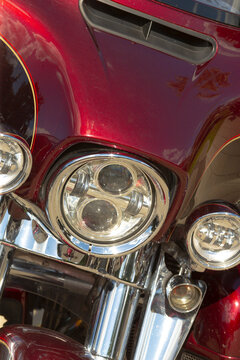 Close-up of motorcycle front showing round headlight assemblies, chrome fork tubes, and glossy maroon painted fairing with reflections.