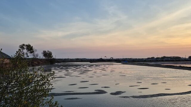 Traditional salt farm pans with mud mounds and water reflections during twilight sunset