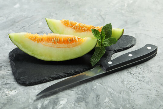 Pieces of ripe melon, knife and mint on grey table, closeup