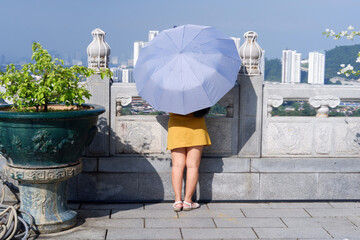 Young woman shielding herself with a parasol from the intense Asian sun at a scenic viewpoint. © Miguel