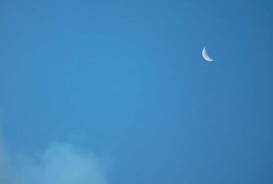 Sharp daytime moon with visible surface craters against a clear blue sky background