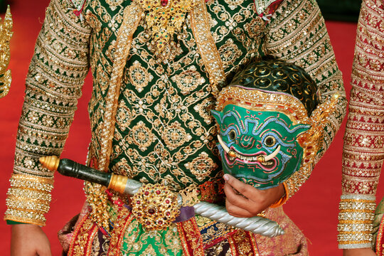 Traditional Thai Khon masked drama artist in elaborate costume holding the giant demon Kumbhakarna's mask in hand