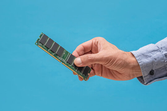 Hand holding a RAM stick. A man in a blue shirt holds a DDR memory module against a vivid blue background. Ideal for tech articles, hardware guides, and IT content.