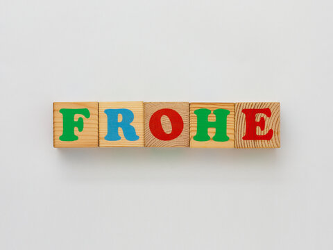 The image features wooden alphabet blocks displaying the German word FROHE, which translates to happy in English