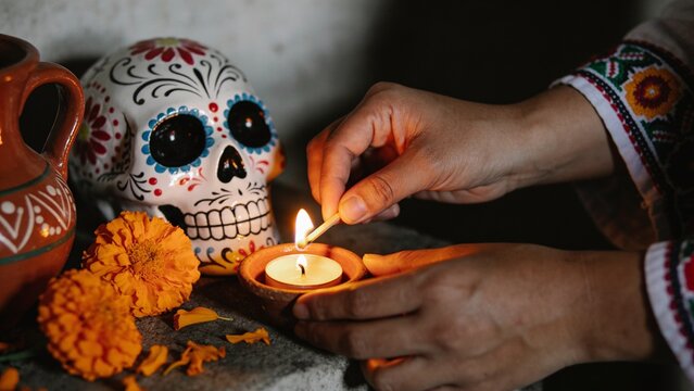 A traditional Mexican D&iacute;a de los Muertos ofrenda altar arranged inside a modest home, with a decorated white sugar skull, orange marigold flowers, lit candles, framed family photographs, oranges, brea