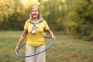 Senior woman exercising with hula hoop outdoors, space for text © New Africa