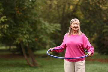 Senior woman exercising with hula hoop outdoors, space for text © New Africa