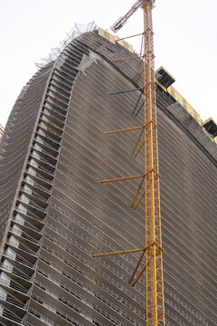 Batumi city development and construction of high-rise skyscrapers using heavy machinery and cranes, skyscraper under construction with safety netting along edges and towering crane reaching top floors
