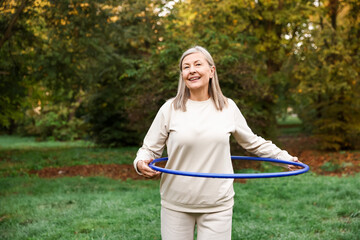 Senior woman exercising with hula hoop outdoors, space for text © New Africa