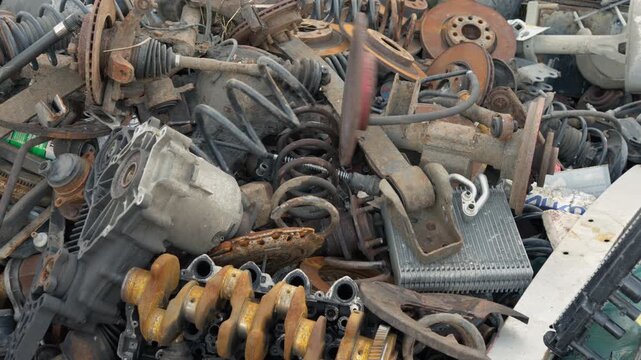 Auto mechanic in gloves throws worn vehicle parts onto a massive scrap pile. Discarded iron clutch discs and springs undergo sorting at salvage scrapyard.