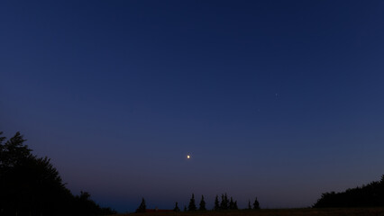 Moon on a twilight sky with stars, planets and landscape mountain silhouettes. © astrosystem