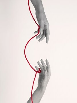 Two hands connected by red string on neutral background  