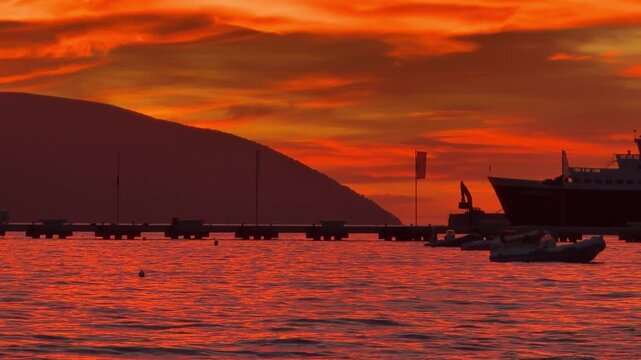 Orange Sunset Over Calm Sea. Cargo Ship Pier And Small Boat Near Mountain Coastline