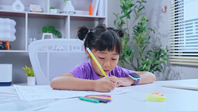 Asian girl focused on writing homework and drawing with colored pencil on table at home
