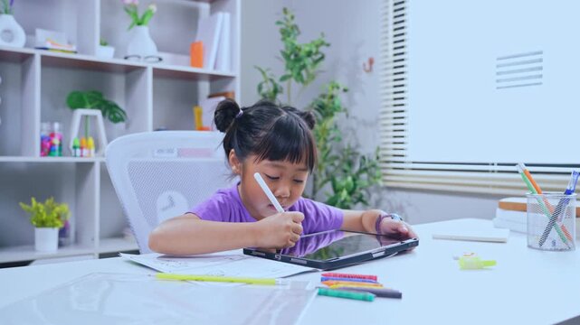 Asian girl drawing on digital tablet with stylus pen at desk in living room for online learning