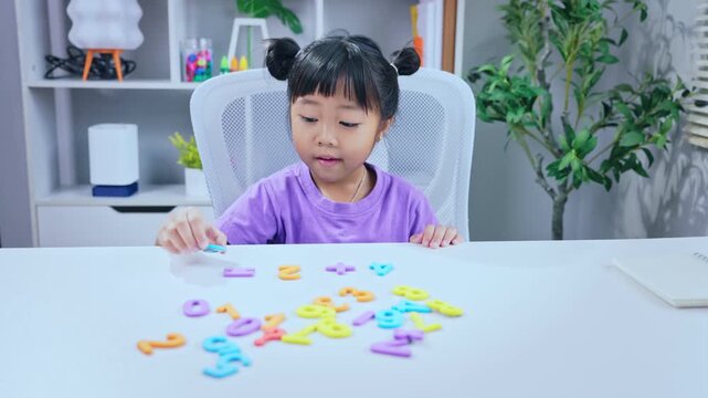 Little asian girl solving math equations using colorful numbers on desk during home schooling education