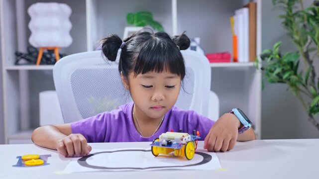 Asian girl testing robotic toy vehicle following line track on classroom desk in stem education concept