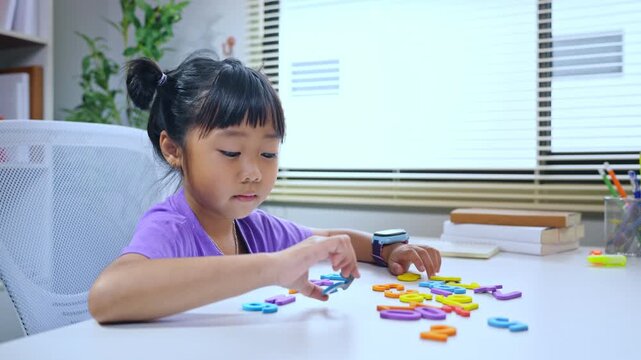 Little asian girl solving math equations using colorful numbers on desk during home schooling education