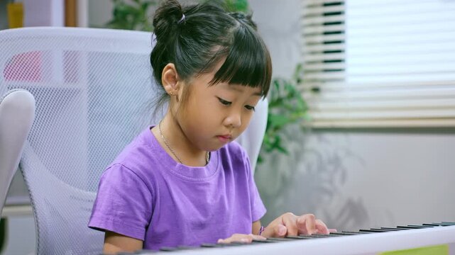 Asian girl practicing piano keyboard at home while smiling and learning musical instrument