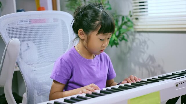 Asian girl practicing piano keyboard at home while smiling and learning musical instrument