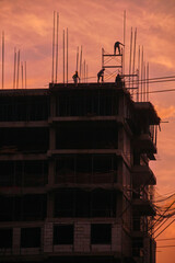 Silhouettes of construction workers building high rise skyscraper against orange sunset sky © Marat