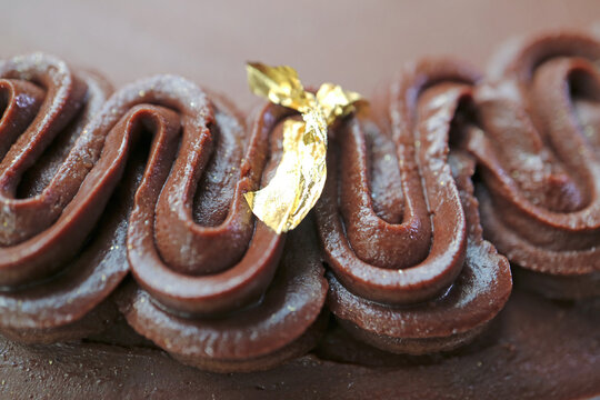 Macro shot of gorgeous dark chocolate ganache frosting on a cake decorated with premium edible gold leaf