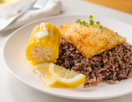 Baked breaded tilapia with wild rice, butter on a corn cob. AI