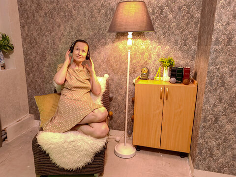 Woman listening to an audiobook through headphones while seated at home. Personal entertainment and audio learning. Relaxation, digital media and private leisure. Cozy indoor lifestyle