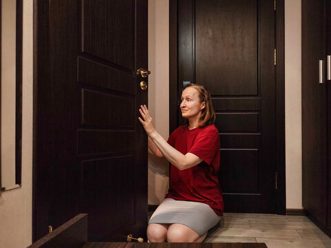 Woman peeking through a partially open bathroom door. Curious woman looking through doorway. Privacy and personal space concept. Home interior and everyday life