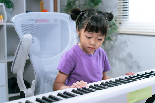 Asian girl practicing piano keyboard at home while smiling and learning musical instrument
