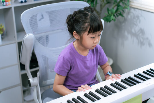 Asian girl practicing piano keyboard at home while smiling and learning musical instrument
