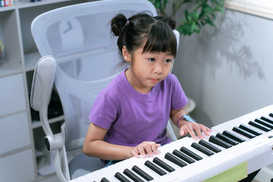 Asian girl practicing piano keyboard at home while smiling and learning musical instrument
