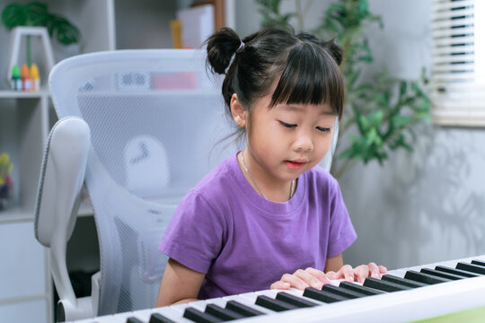 Asian girl practicing piano keyboard at home while smiling and learning musical instrument
