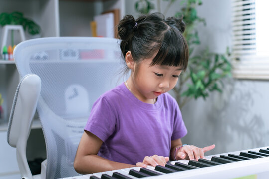 Asian girl practicing piano keyboard at home while smiling and learning musical instrument
