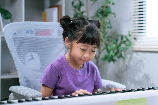 Asian girl practicing piano keyboard at home while smiling and learning musical instrument

