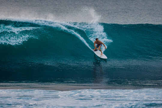 Surfer man riding on surfboard while and carving through a blue wave with water spray