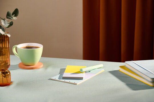 A serene desk setup with a cup of coffee, notebooks, and a vase