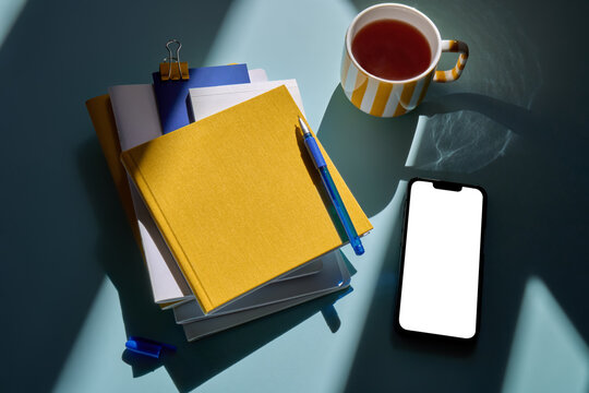 Smartphone With Blank Screen, Yellow Notebook, Stationery and Tea Cup.