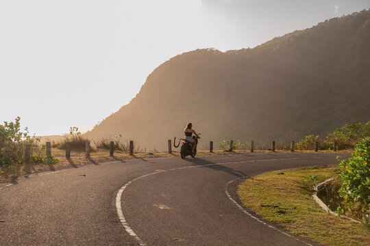 Anonymous woman riding scooter on coastal road at sunset