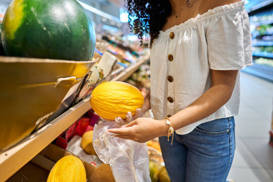 Woman buying fresh melon in supermarket produce aisle