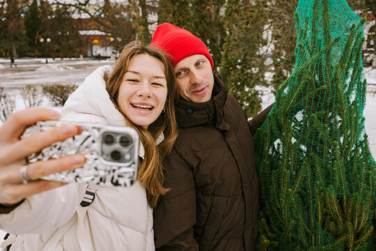 A man and a woman are taking a selfie with a Christmas tree.