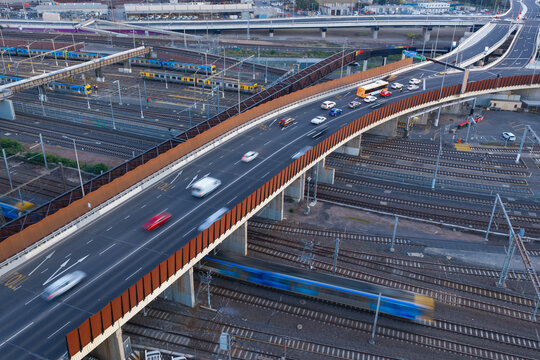 Traffic on a freeway on ramp above commuter trains in a railway yard