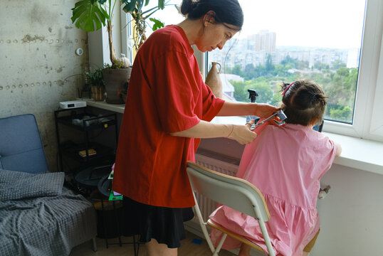 Mother carefully cutting her son's hair by the window.