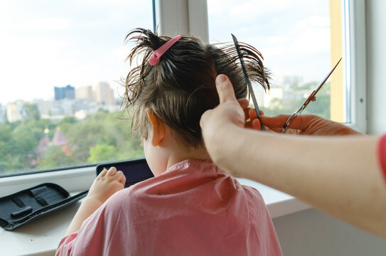 Mother using scissors and a comb to cut her son's hair.