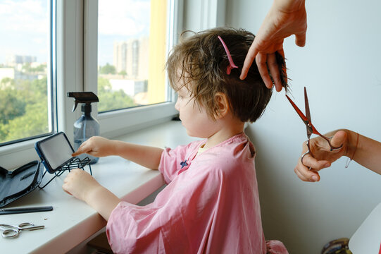 Mother using scissors to cut a section of her son's hair.