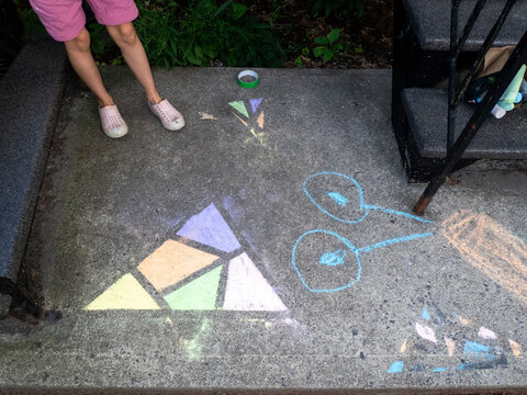 Child drawing colorful chalk art on a concrete garden step