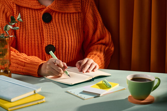 Person writing in a notebook with a cup of coffee and eucalyptus on