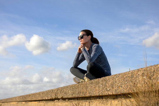 Woman in Sportswear Sitting Resting and Reflecting on a Coastal Wall