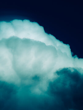 Surreal teal and deep navy cumulus cloud glowing against a dark midnight blue sky, moody stylized cloudscape background with dramatic tones and copy space