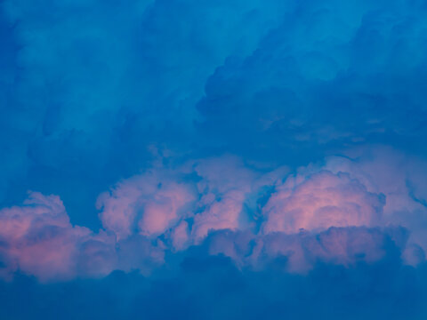 Soft pink tinted clouds glowing at the bottom of a vivid blue sky at dusk, dreamy pastel cotton candy cloudscape background